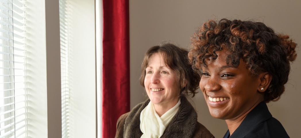 Sanctuary residents looking out of a window with open blinds and a red curtain and smiling