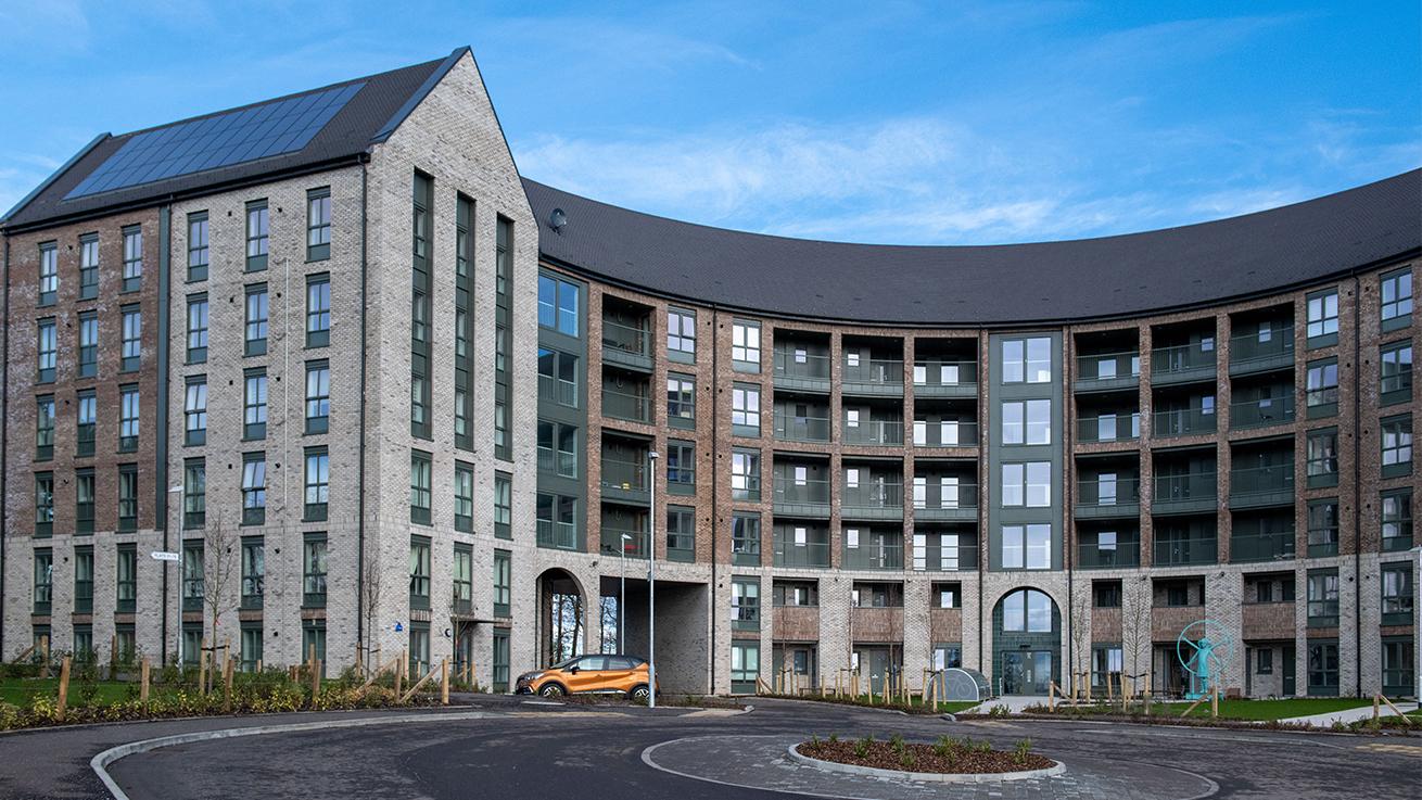 Exterior of a curved block of flats built using grey brick with a roundabout in the foreground