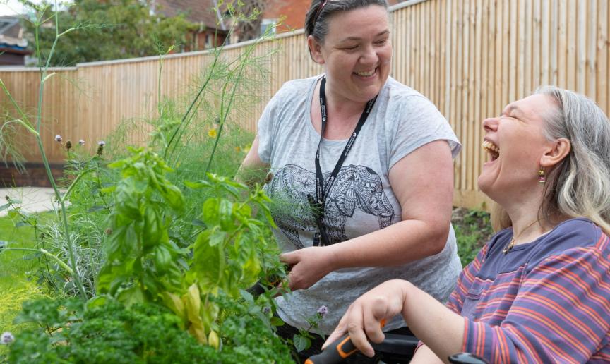 A Sanctuary Supported Living member of staff and a resident in a wheelchair laughing together whilst doing gardening