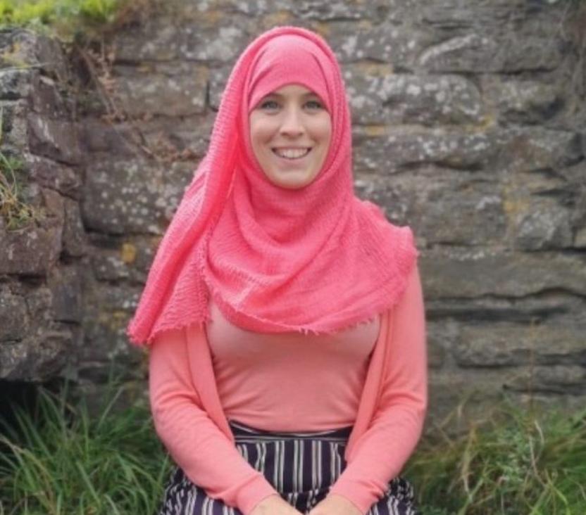 A smiling woman sat outside wearing a headscarf